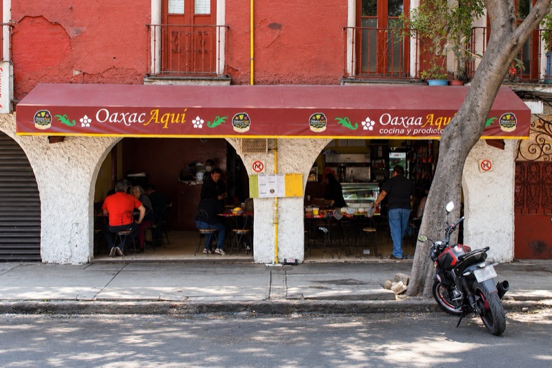 Fachada de Oaxacaquí en Santa María la Ribera: toldo guinda con el logo, arcos blancos y comensales en las mesas